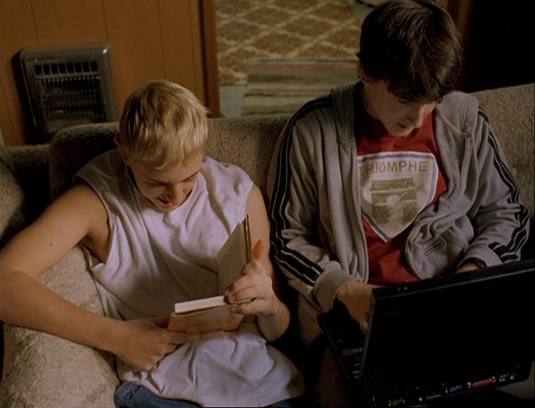 a boy and a girl sitting on a couch looking at a book