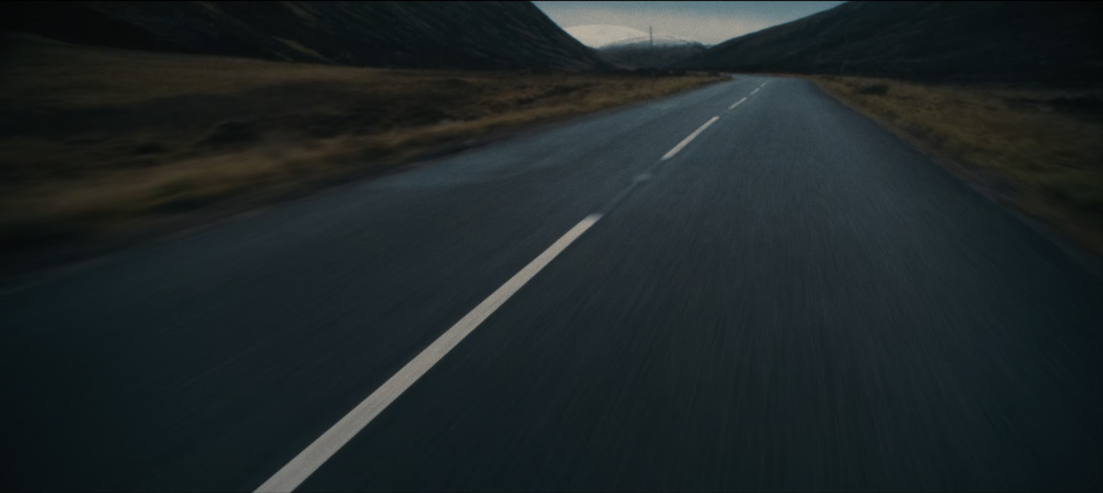 a car driving down a road with mountains in the background