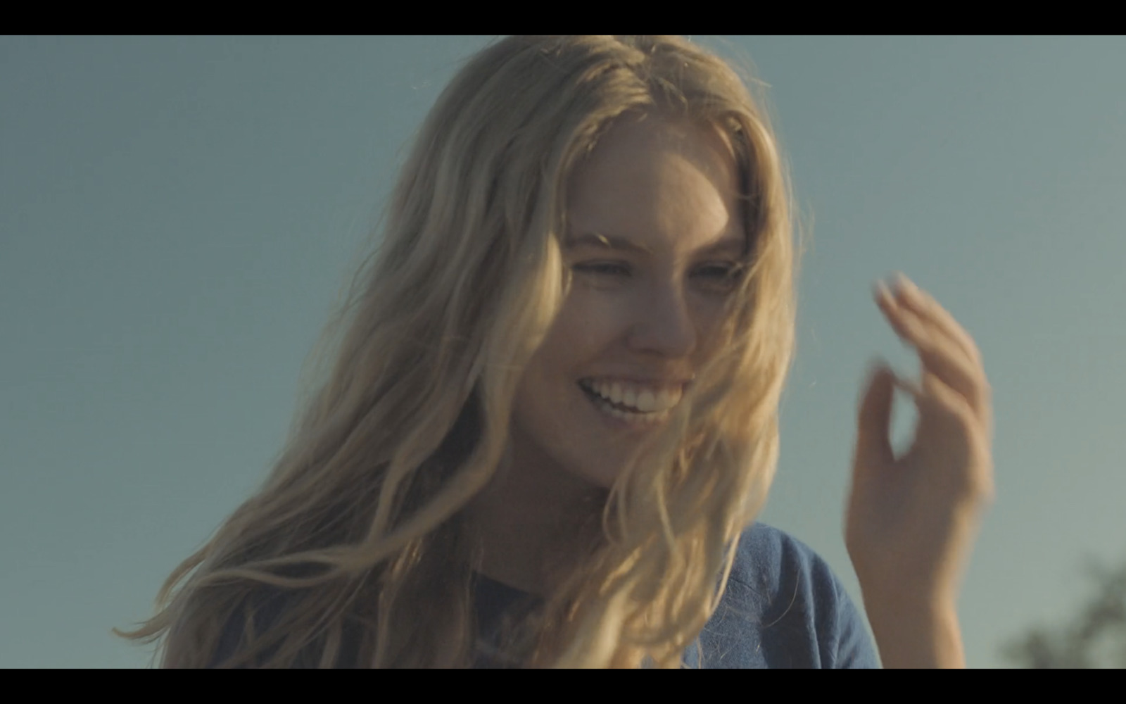 a woman with long blonde hair smiling and waving