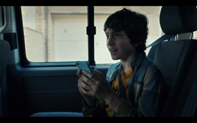 a young boy sitting in the back seat of a car looking at a cell phone