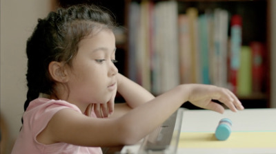 a little girl sitting at a table using a laptop computer