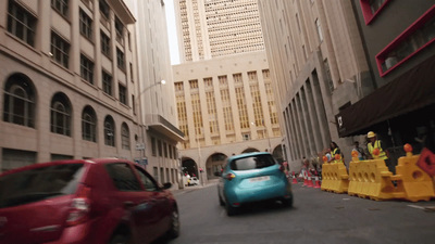 a blue car driving down a street next to tall buildings