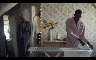 a woman ironing clothes in a room with floral wallpaper