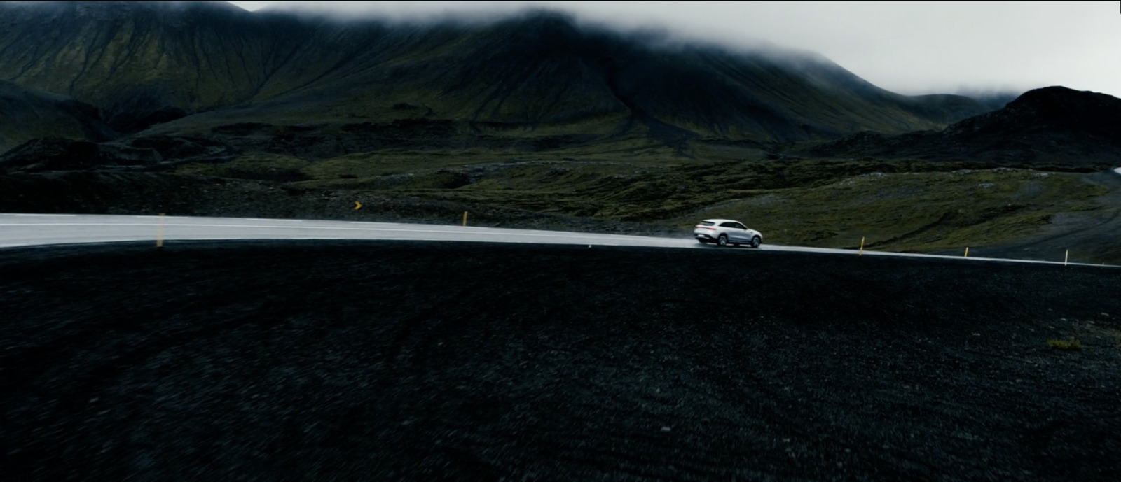 a white car driving down a road next to a mountain