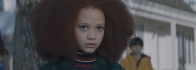 a young girl with an afro standing in front of a building