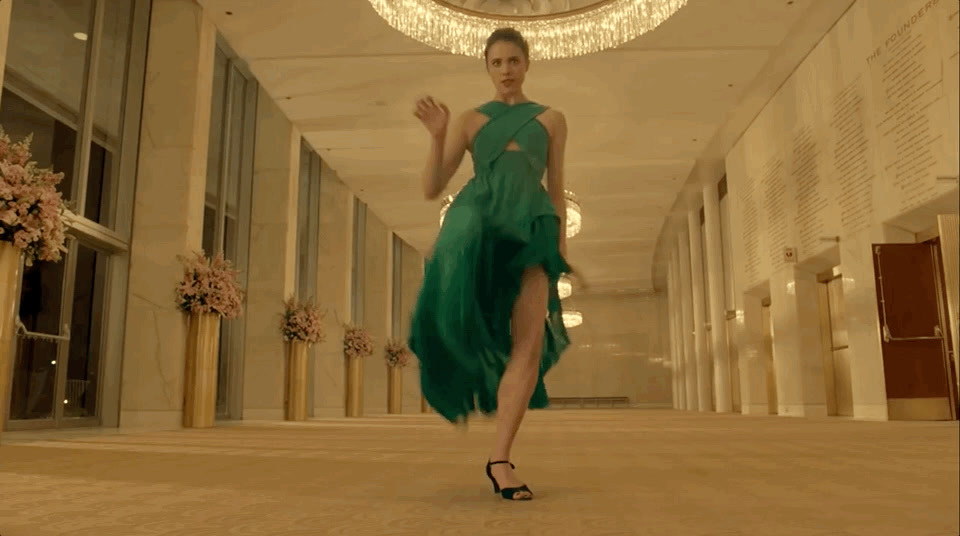 a woman in a green dress walking down a hall