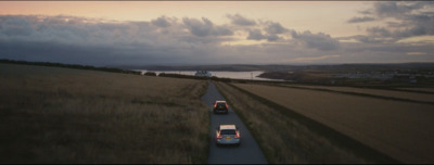 a couple of cars driving down a road next to a field