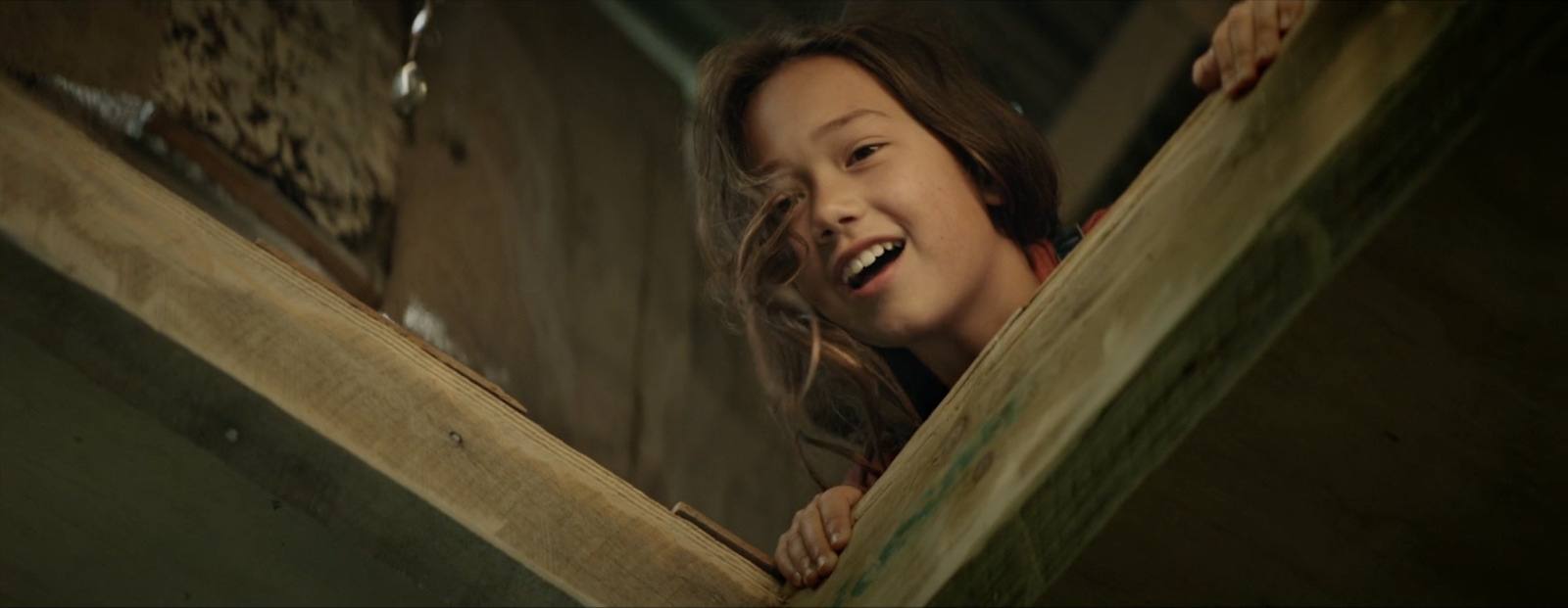 a young girl is smiling while looking out from a wooden structure