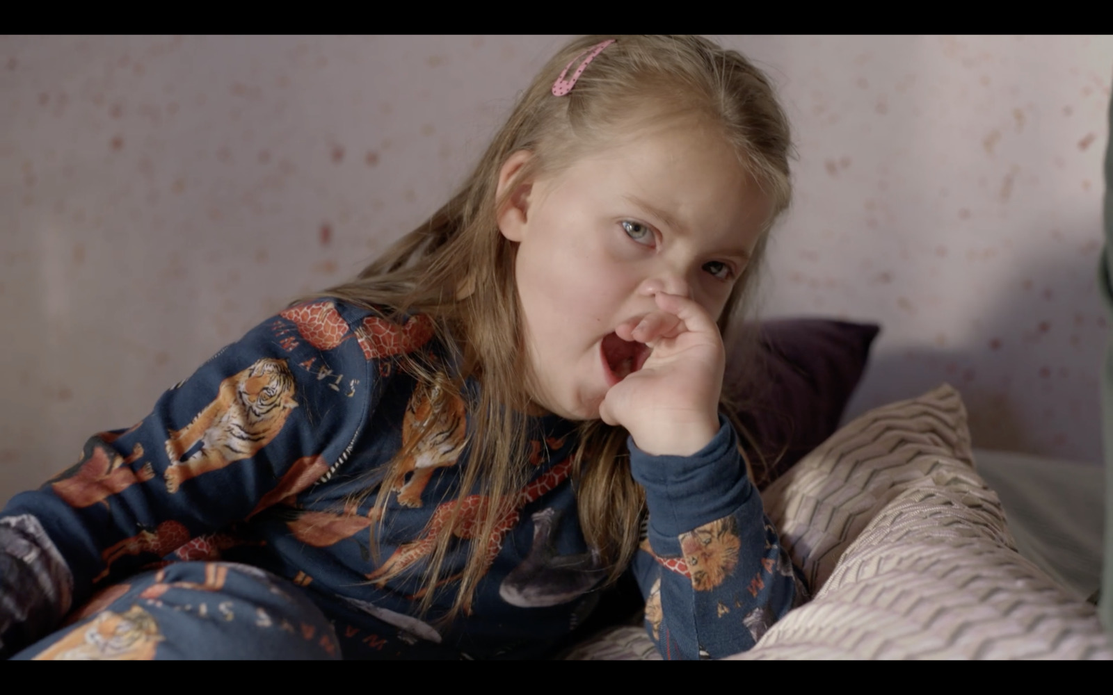 a little girl sitting on a bed with her hand in her mouth