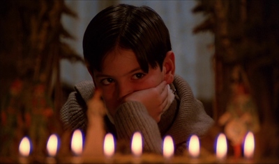 a young boy sitting in front of a bunch of lit candles