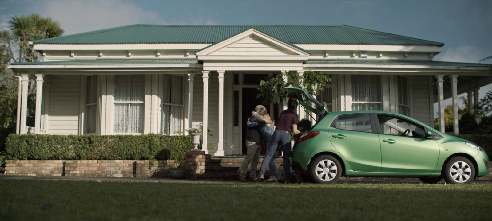 a green car parked in front of a white house