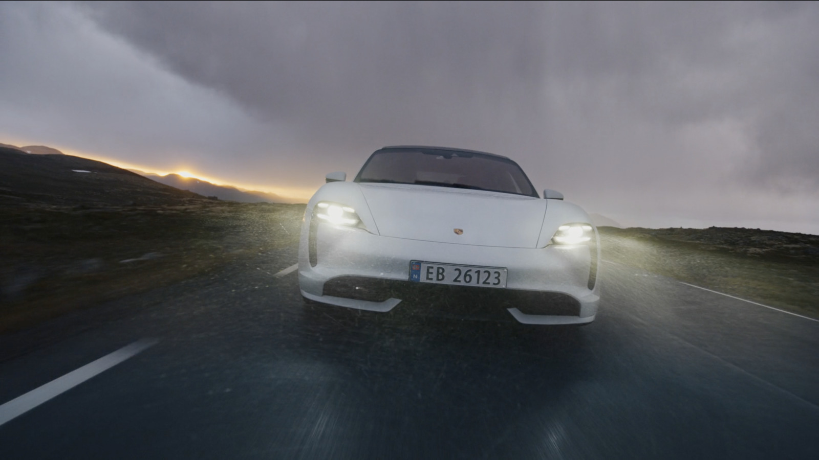 a white car driving down a road under a cloudy sky