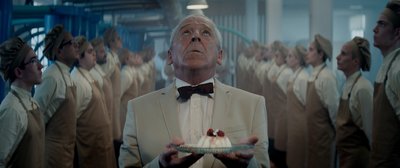 a man in a tuxedo holding a cake in front of a group of