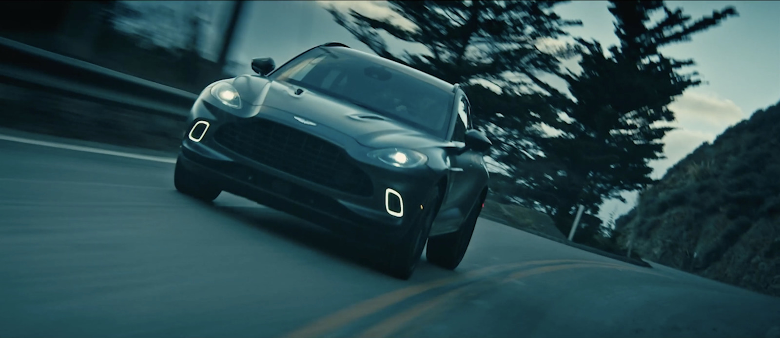 a black car driving down a road next to a forest