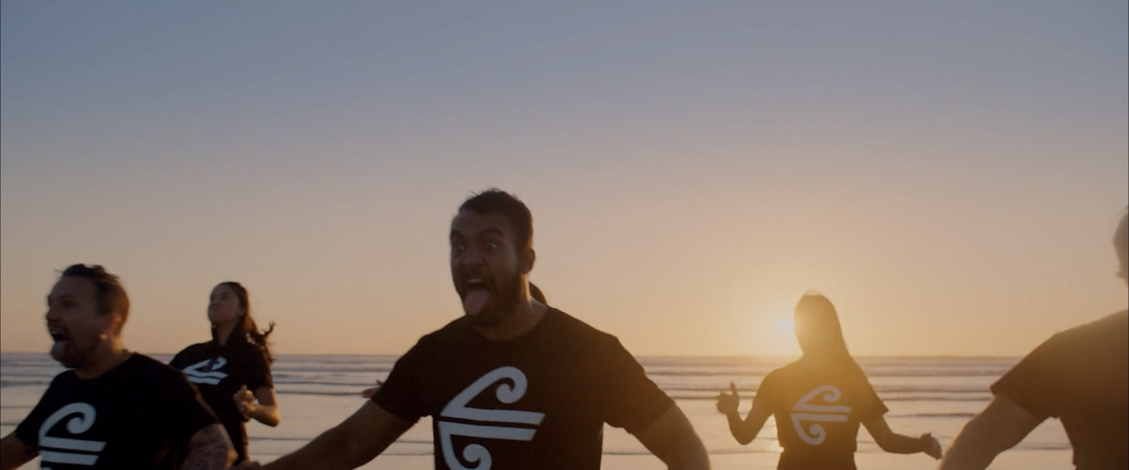 a group of people running on a beach at sunset