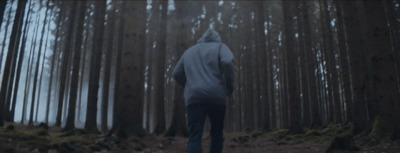 a person in a hooded jacket walking through a forest