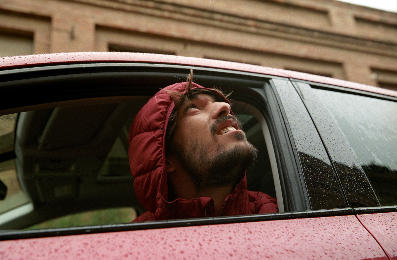 a man in a red jacket looking out of a car window