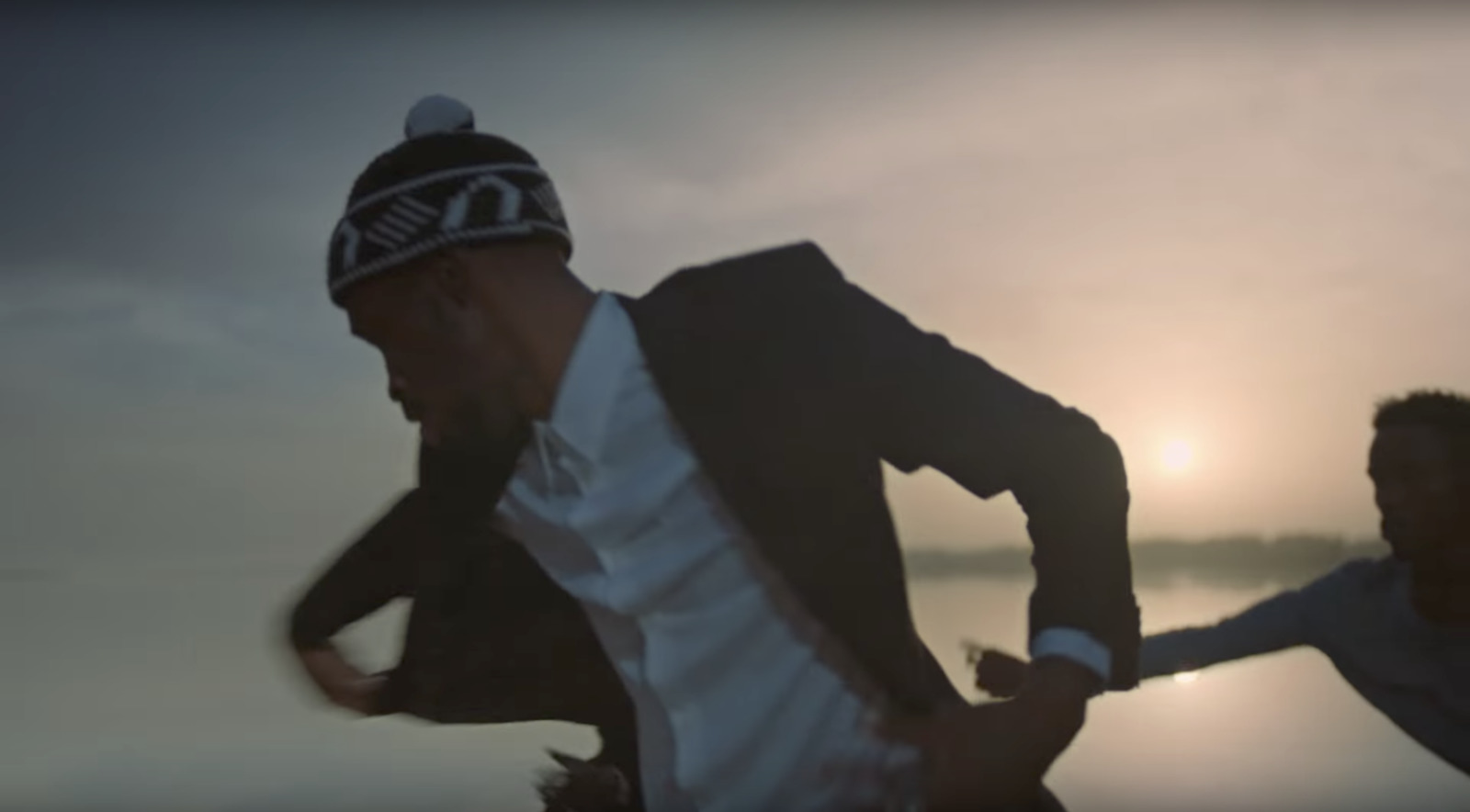 a man in a suit and hat running on the beach