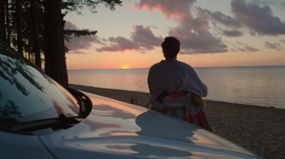 a man standing next to a parked car on a beach