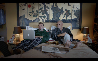 a man and a woman sitting on a bed looking at a laptop