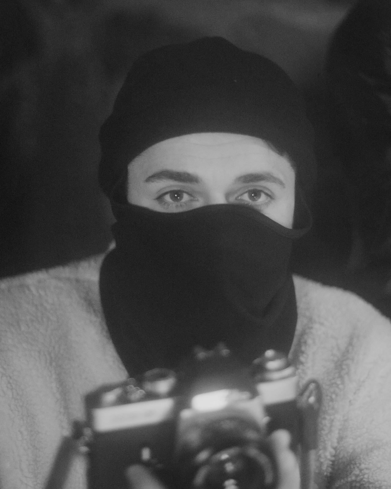 a woman wearing a black hat and a black scarf holding a camera