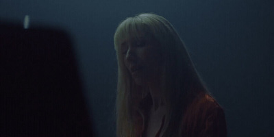 a woman with long blonde hair standing in a dark room