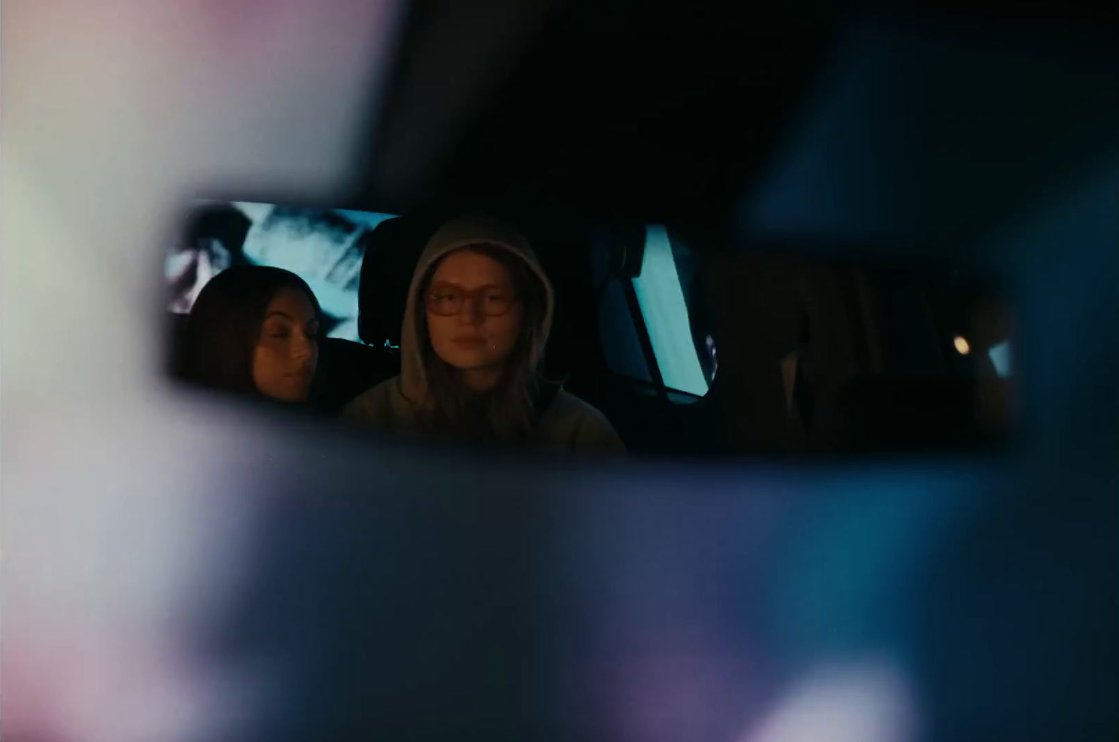 a woman sitting in a car looking at her reflection in a rear view mirror