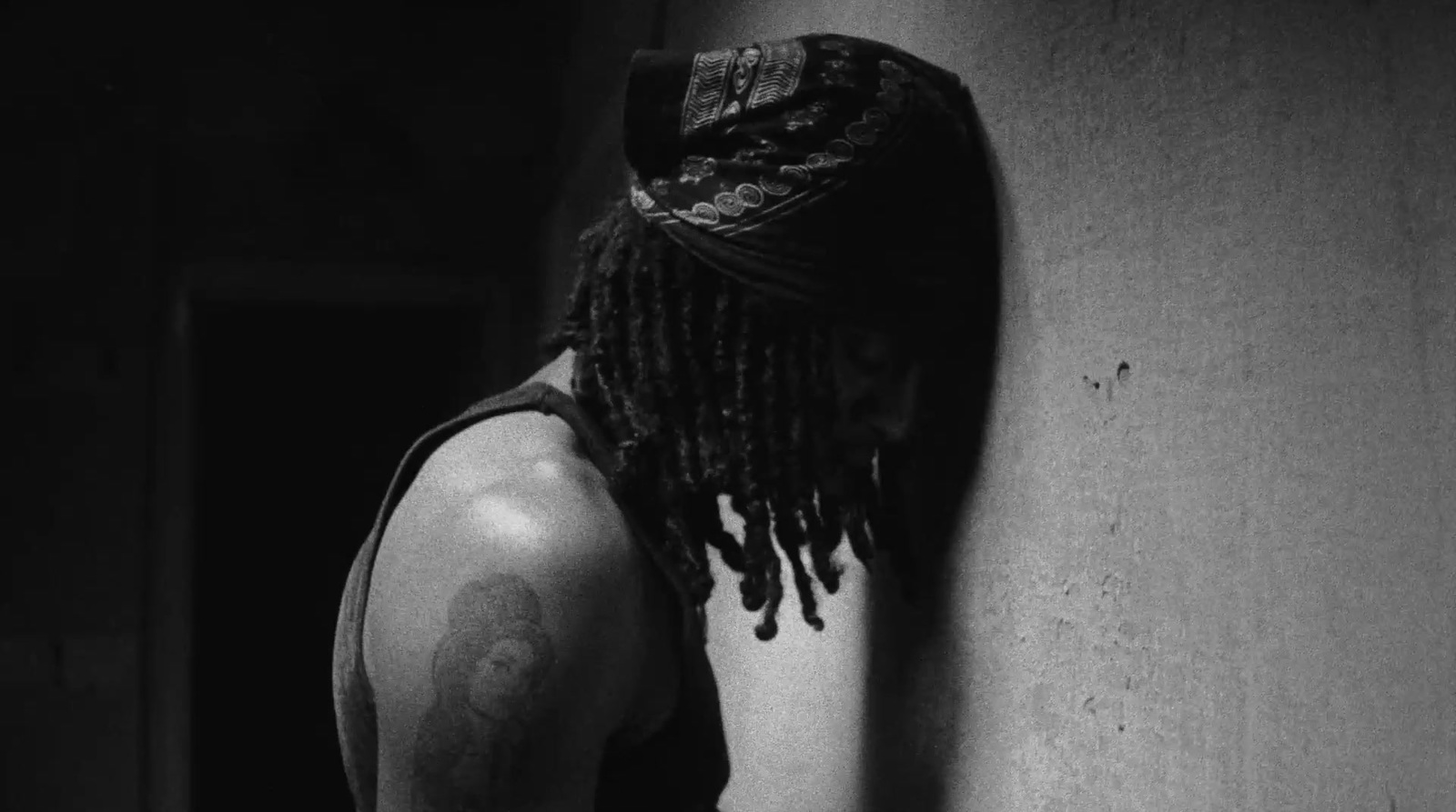 a man with dreadlocks leaning against a wall