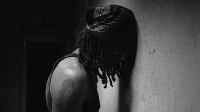 a man with dreadlocks leaning against a wall