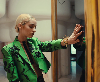 a woman in a green jacket is looking in a mirror