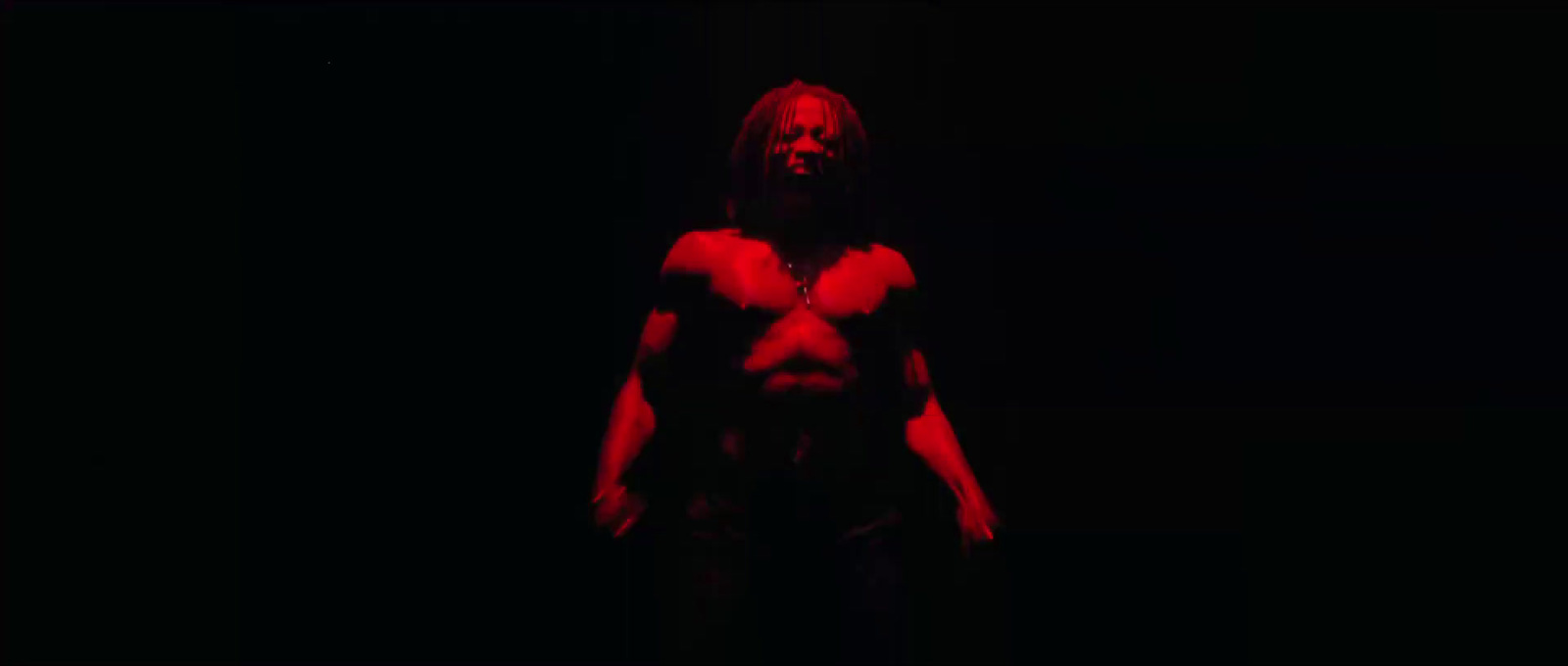 a man with long hair and no shirt standing in the dark