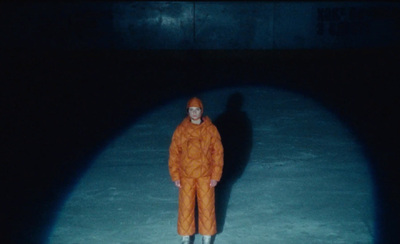 a man in an orange jumpsuit standing in the dark