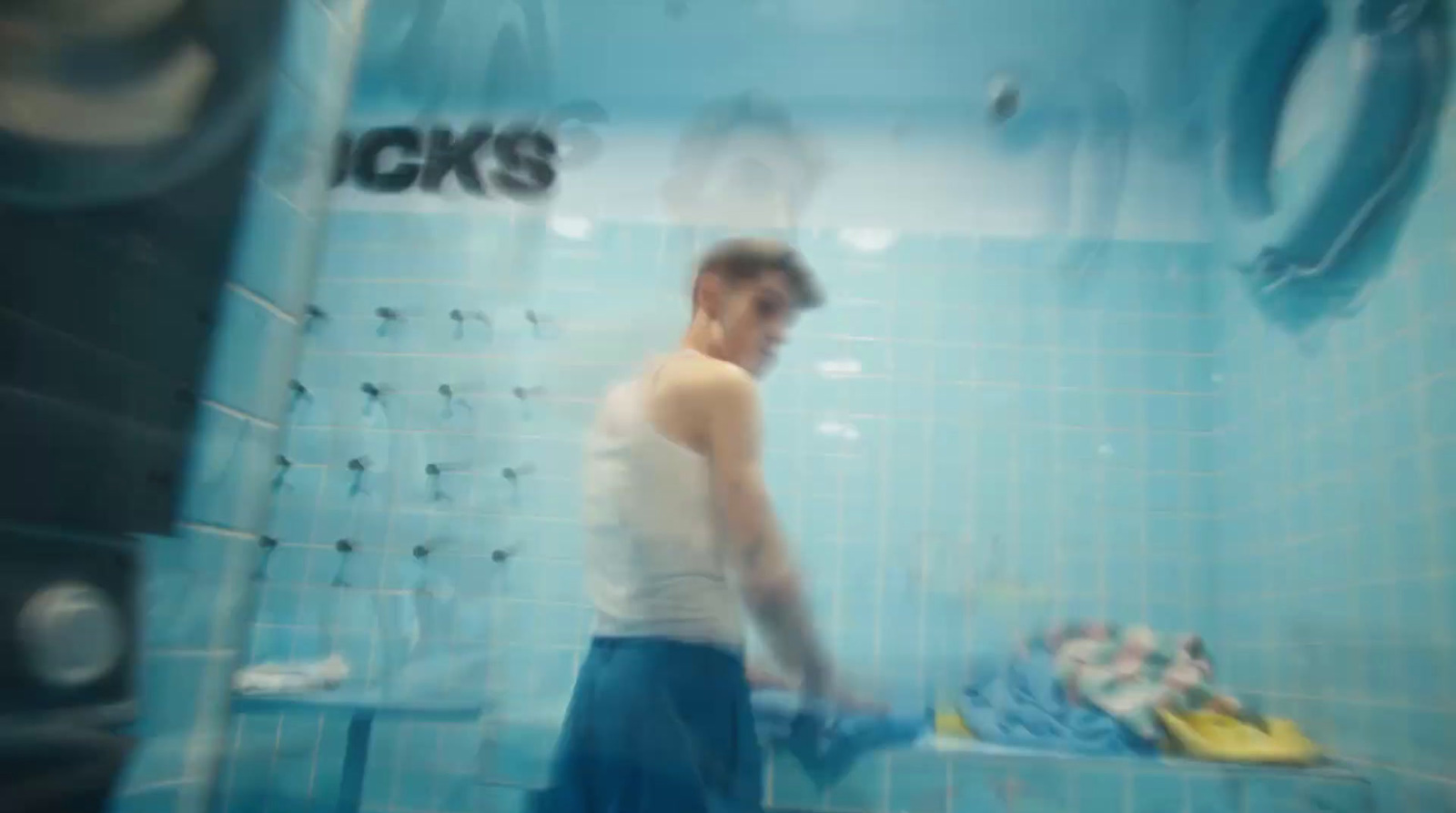 a man in a white tank top in a blue tiled bathroom