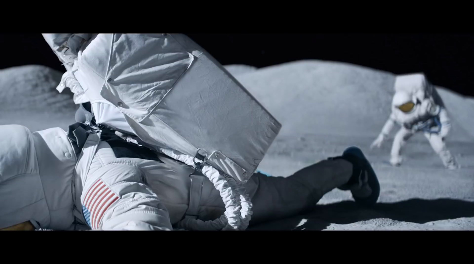 a man laying on the moon with an astronaut in the background