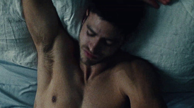 a shirtless man laying on a bed with his hands on his head