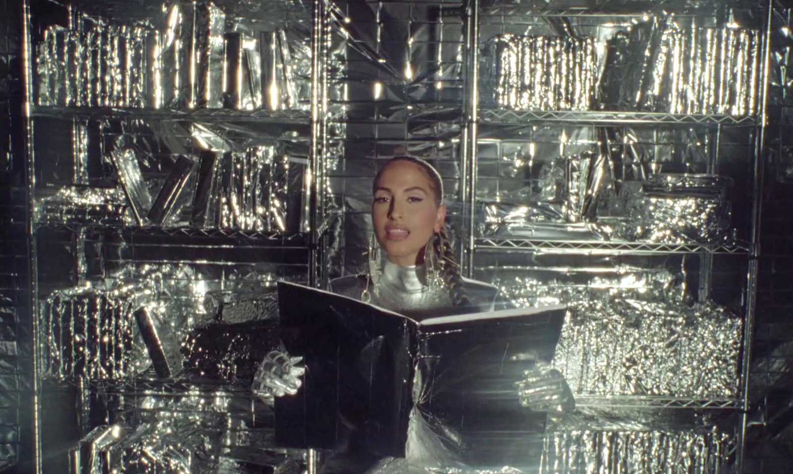 a woman is reading a book in front of a wall of shiny objects