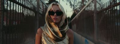 a woman wearing sunglasses and a scarf walking down a street