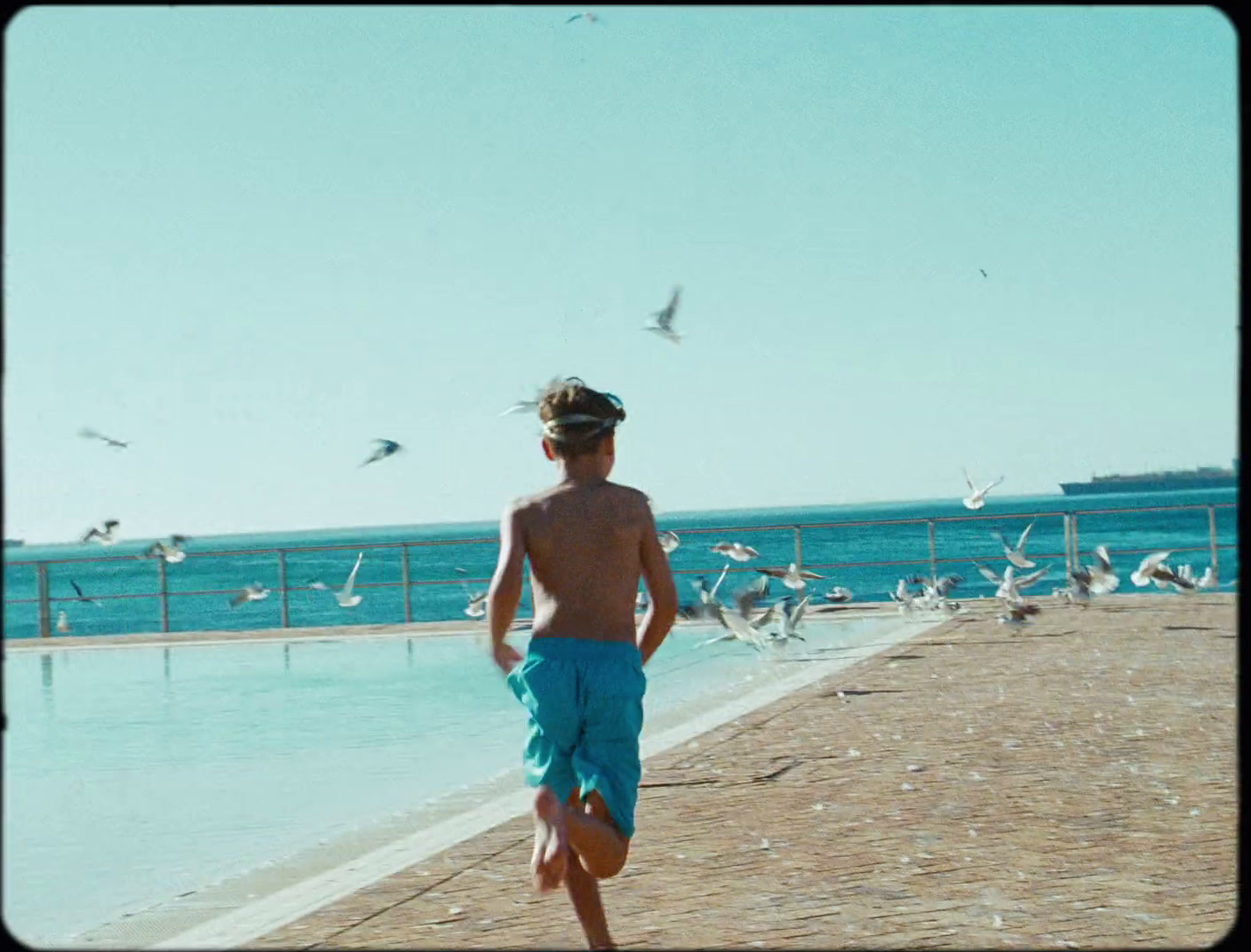 a young boy standing on a beach next to a body of water