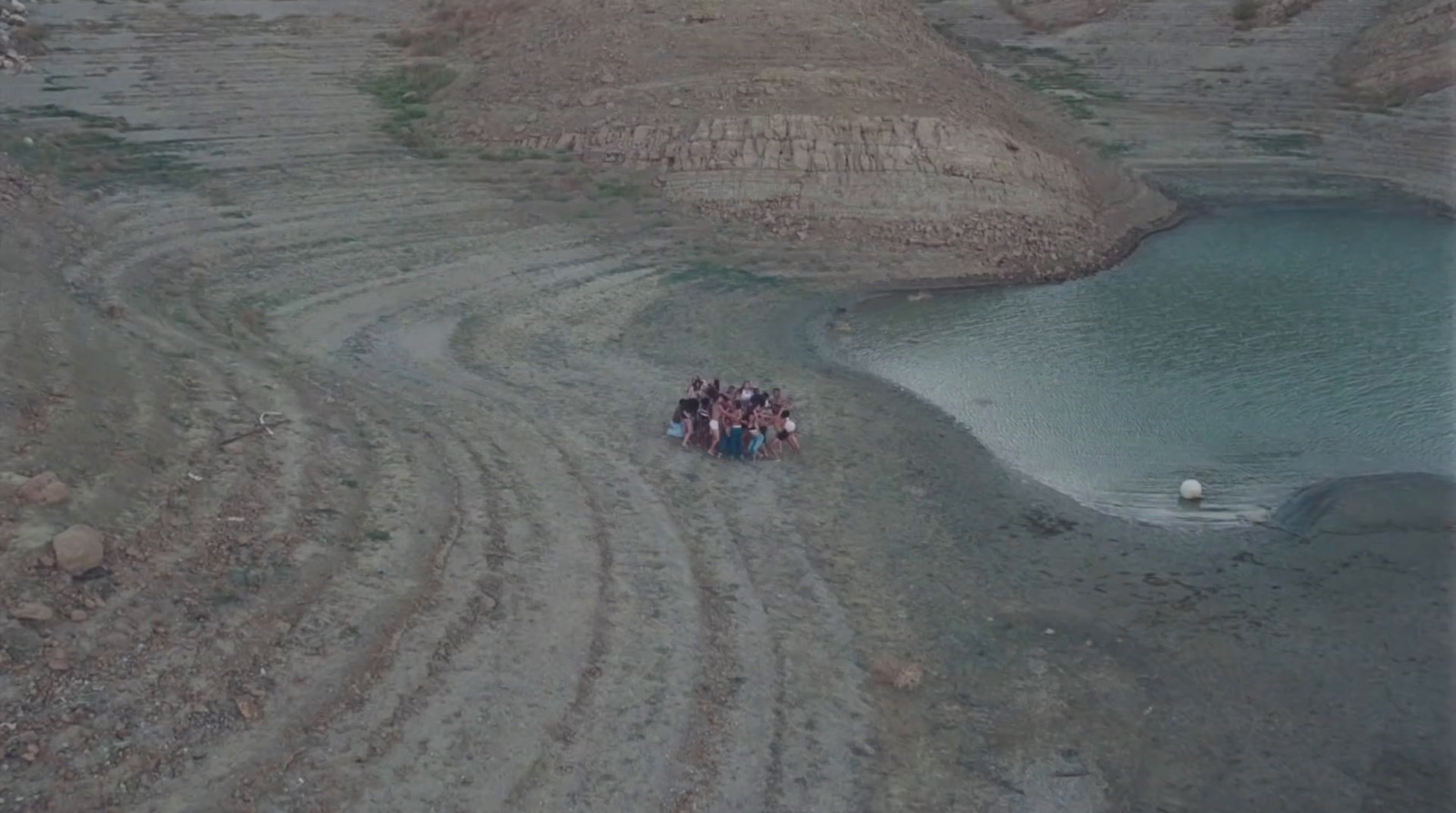 a group of people standing on a dirt road next to a body of water