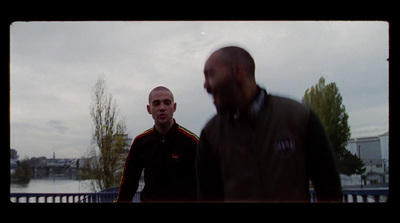 two men standing next to each other in front of a body of water