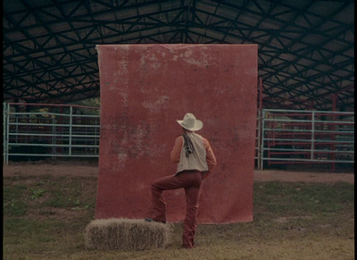 a man standing on a hay bale in front of a red wall