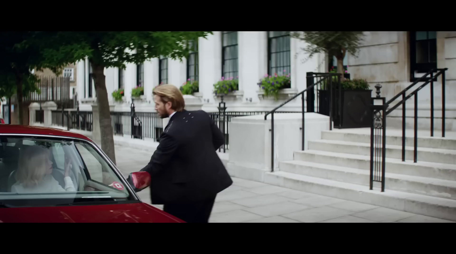 a man in a suit and tie standing next to a red car