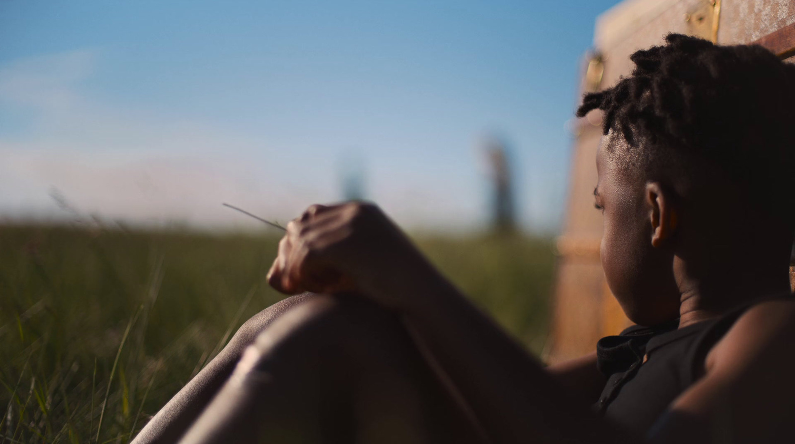 a woman sitting in the grass with a suitcase in the background