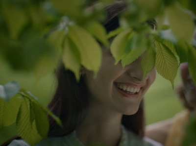 a woman is smiling and looking through the leaves of a tree