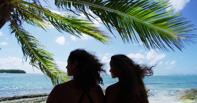 a couple of women standing next to each other under a palm tree