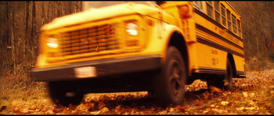 a yellow school bus driving down a leaf covered road