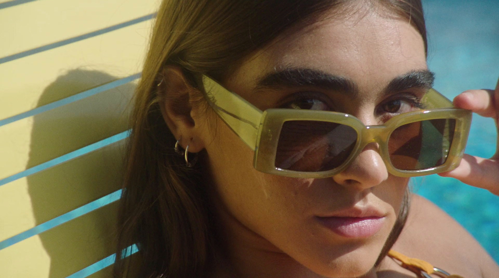 a woman wearing sunglasses is leaning against a wall