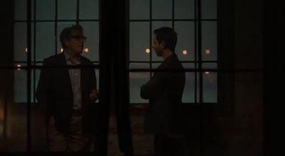 a couple of men standing next to each other in front of a window