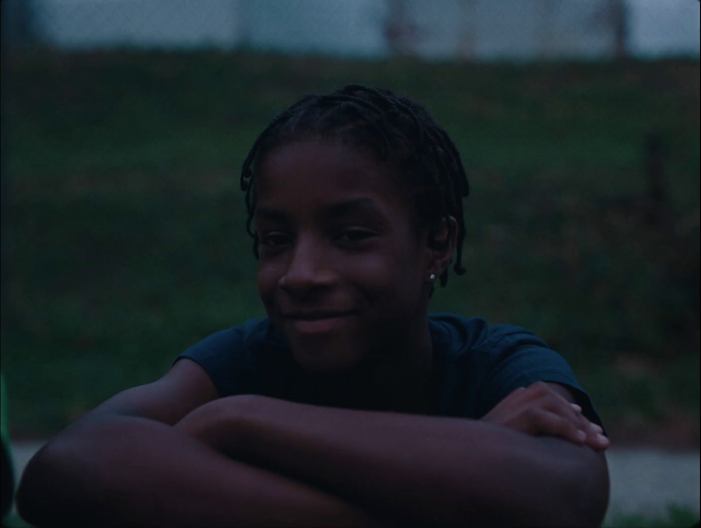 a young girl with dreadlocks sitting in the grass