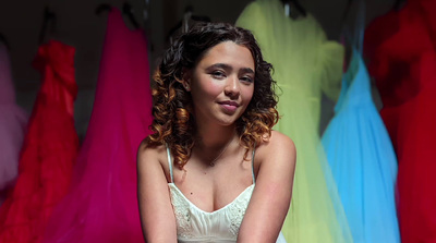 a woman sitting in front of a rack of dresses